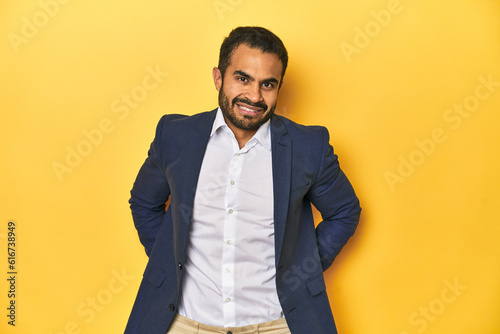 Professional young Latino man in business suit, yellow studio background, happy, smiling and cheerful.