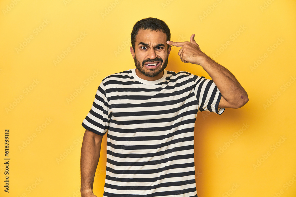Casual young Latino man against a vibrant yellow studio background, showing a disappointment gesture with forefinger. Casual young Latino man against a vibrant yellow studio background, showing a disappointment gesture with forefinger.