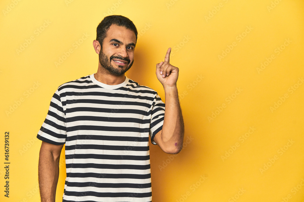 Casual young Latino man against a vibrant yellow studio background, showing number one with finger. Casual young Latino man against a vibrant yellow studio background, showing number one with finger.