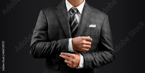 Confident Handsome Young Man In Dark Checks Suit Adjusting cuff Isolated On Dark Background