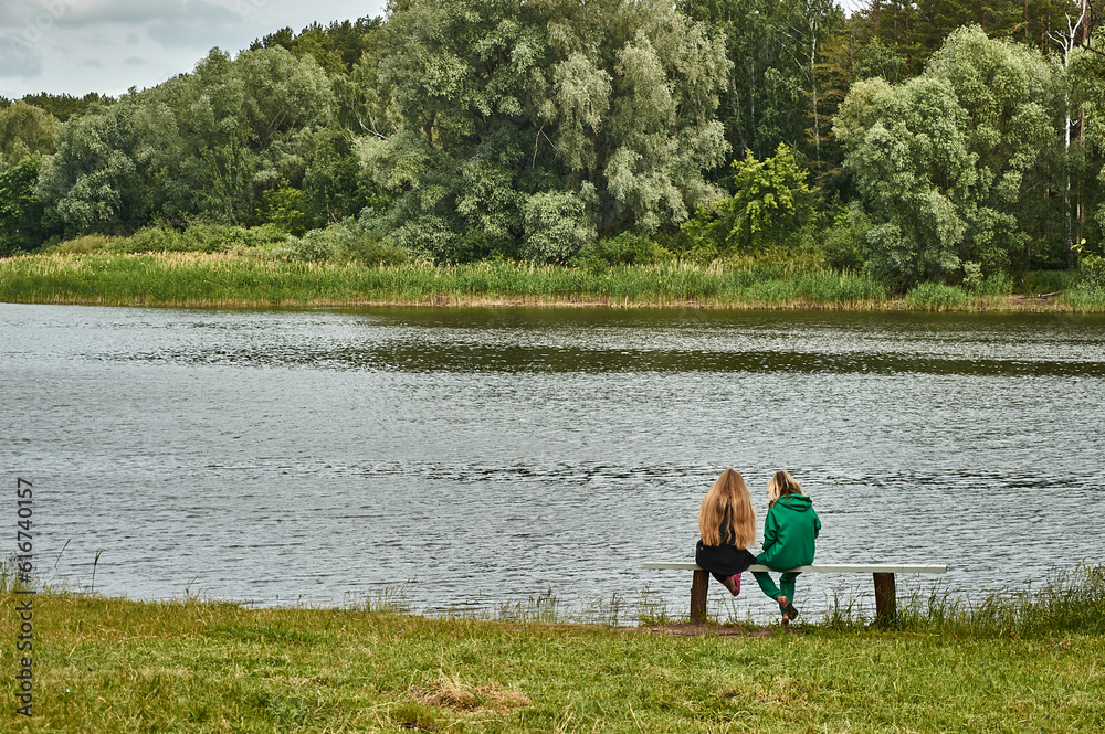 Two girls are sitting on a bench on the shore of the bay Two girls are sitting on a bench on the shore of the bay