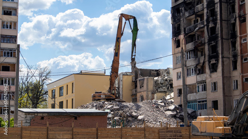 Facade of a residential abandoned multi-storey building after a strong fire. A construction excavator with a hydraulic crusher demolishes a house for repairs. The collapse of a residential building.