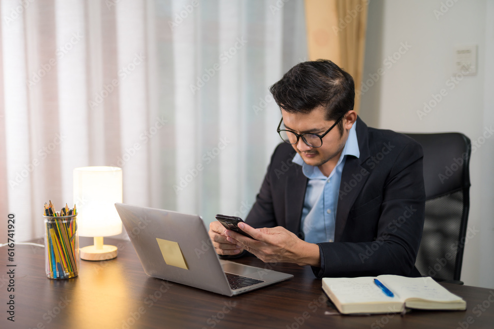 Asian businessman is using smartphone to check messages on desk with laptop at home. Asian businessman is using smartphone to check messages on desk with laptop at home.