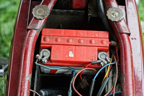 Fototapeta Naklejka Na Ścianę i Meble -  one old plastic lead small electrolytic red battery with metal terminals and wires is in an old motorcycle on the street
