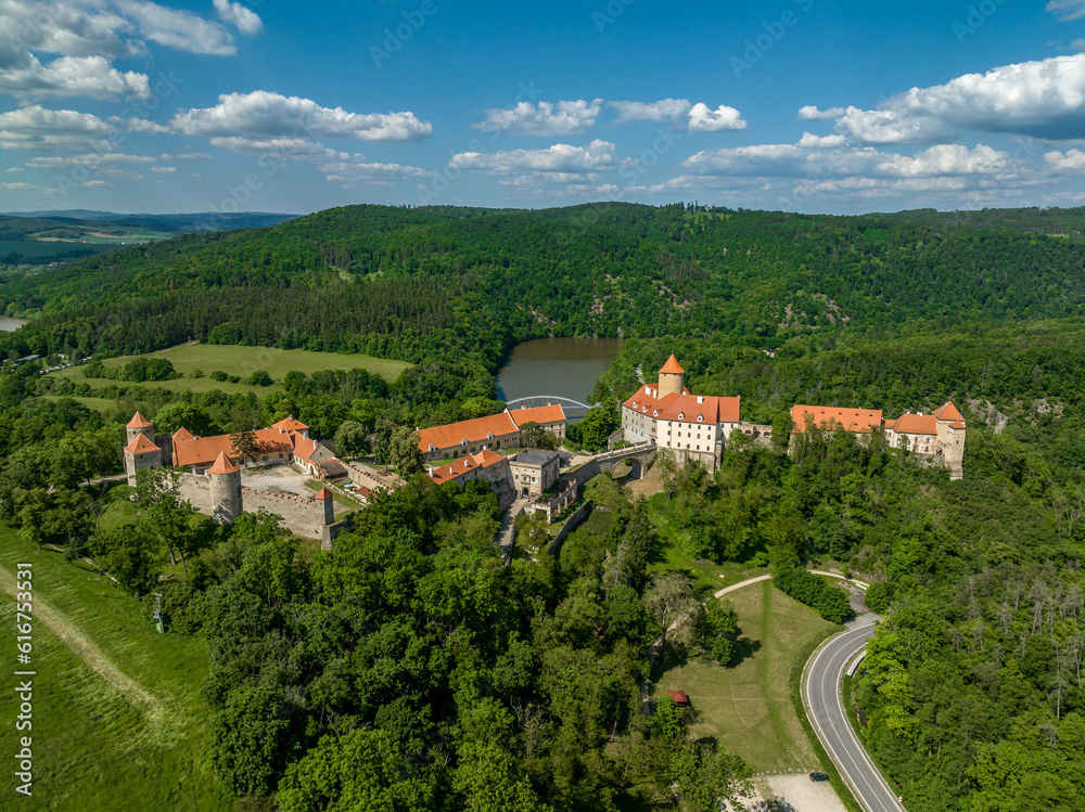 Aerial view of Veveri castle in Moravia with large courtyards, multiple gates, square and round towers with cloudy blue sky 