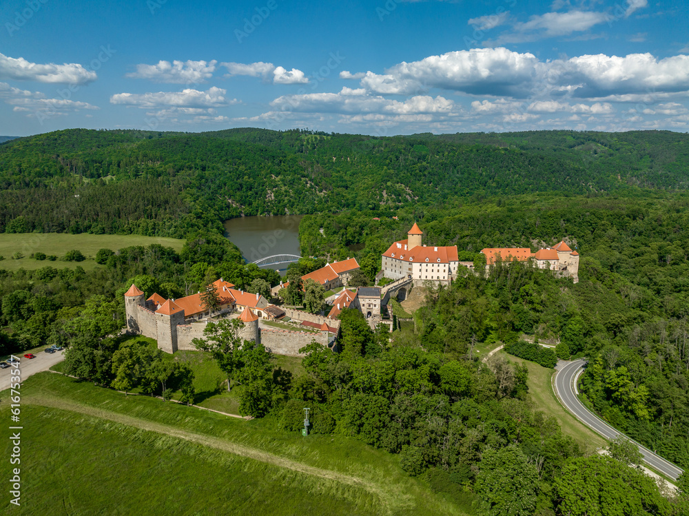 Aerial view of Veveri castle in Moravia with large courtyards, multiple gates, square and round towers with cloudy blue sky 