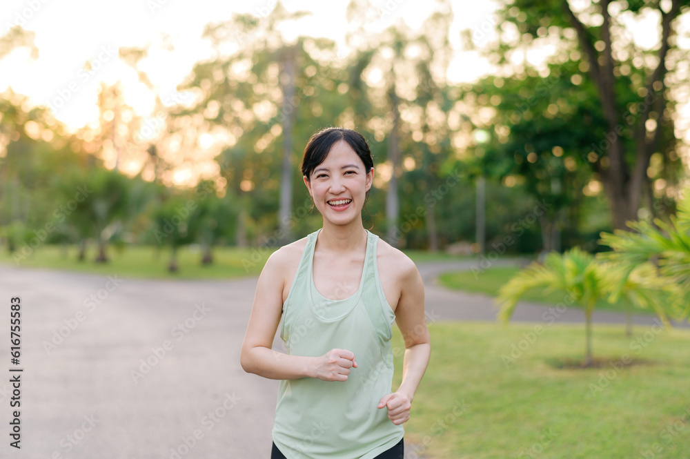 Fit Asian young woman jogging in park smiling happy running and enjoying a healthy outdoor lifestyle. Female jogger. Fitness runner girl in public park. healthy lifestyle and wellness being concept Fit Asian young woman jogging in park smiling happy running and enjoying a healthy outdoor lifestyle. Female jogger. Fitness runner girl in public park. healthy lifestyle and wellness being concept