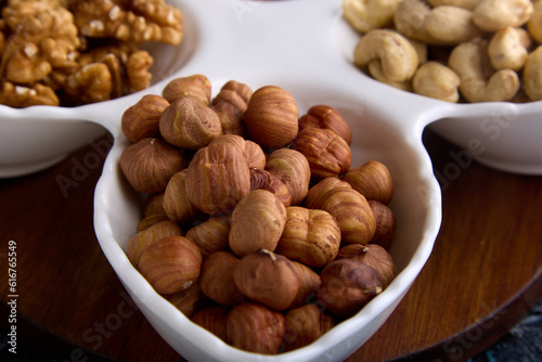 Close-up of healthy hazelnuts in a beautiful white porcelain dish with other nuts. Assorted roasted and dried nuts are laid out in close-up on a white platter
