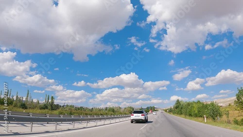 The car is travelling on the motorway separating the oncoming lane with a bollard. The sky is blue with clouds. Timelapse. Flight effect. A road trip photo