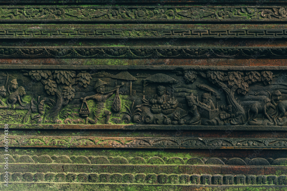 Close up shot of carved stone wall with moss in sacred monkey forest. Balinese architecture carving stone with monkeys scene