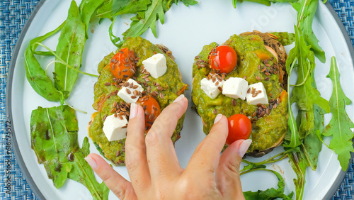 Chef woman hand put a cherry tomato on avocado toast made with fresh ingredients like greek cheese, cherry tomatoes, and mashed avocado on rye bread. A perfect choice for a healthy breakfast or lunch.