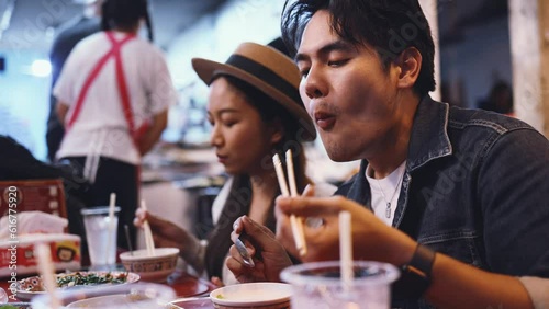 Young Asian couple traveler tourists eating Thai street food together in China town night market in Bangkok, Thailand