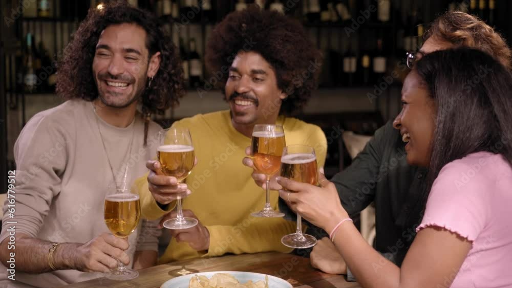 Group of hispanic people partying and drinking beer in a pub. Young multiracial friends having fun in a bar. They chat and laugh. The African American woman looking at camera Group of hispanic people partying and drinking beer in a pub. Young multiracial friends having fun in a bar. They chat and laugh. The African American woman looking at camera