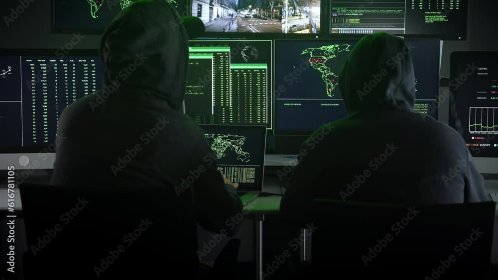 Two hooded hackers work together with computer viewing maps and data on ...
