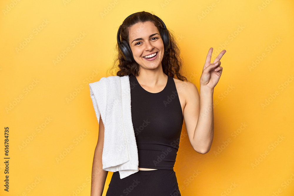 © Asier - Athletic woman holding a towel, yellow background, joyful and carefree showing a peace symbol with fingers. © Asier - Athletic woman holding a towel, yellow background, joyful and carefree showing a peace symbol with fingers.