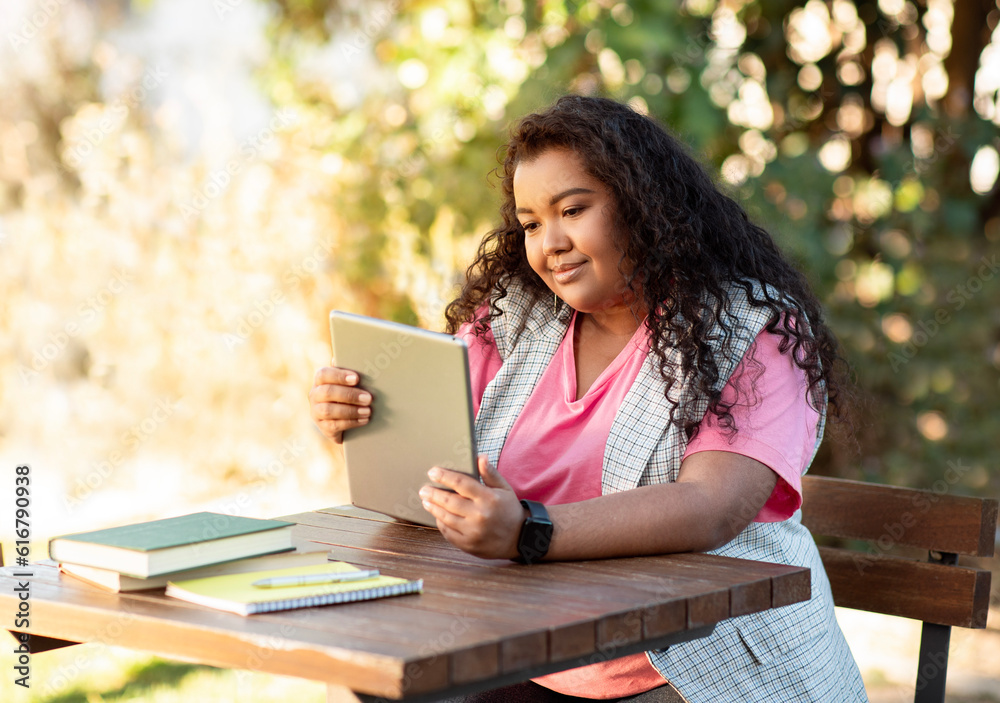Obraz premium Happy mixed woman holding digital tablet studying online websurfing outdoors