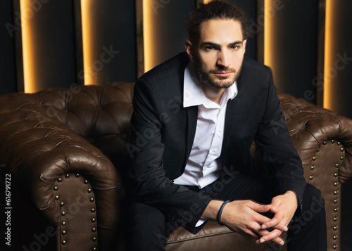 Confident Arabic Businessman Sitting In Armchair In Dark Luxury Interior