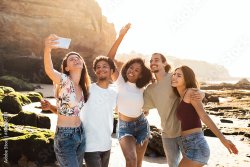 Happy millennial multiethnic people students enjoy summer holidays, have fun, taking selfie on phone
