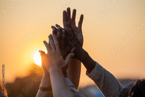Multiracial group of diverse young people giving high five against a setting sun, feels excited close up focus on stacked palms during golden hour. Respect and trust, celebration and friendship