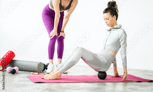 Fototapeta Naklejka Na Ścianę i Meble -  Slim woman training with yoga coach. Private lessons with personal trainer, fitness instructor. Workout, exercises at home on fitness mat. Sports equipment, resistance rubber, massage peanut ball