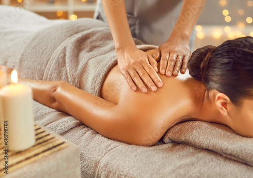 Young woman getting shoulder massage in spa salon. Relaxed brunette girl lying on massage bed during spa treatment procedure. Beauty, skin and body care, wellbeing