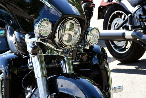 headlight closeup of popular large American made motorcycle. glass lens and shiny chrome finish. mud guard and stainless telescope cylinders. signal lights. bike front detail. wheel and exhaust beyond