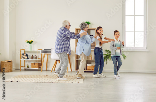 Happy family spending time at home and having fun together. Funny grandparents and children play games and dance conga line. Little kids with granny and granddad walk in line like train in living room