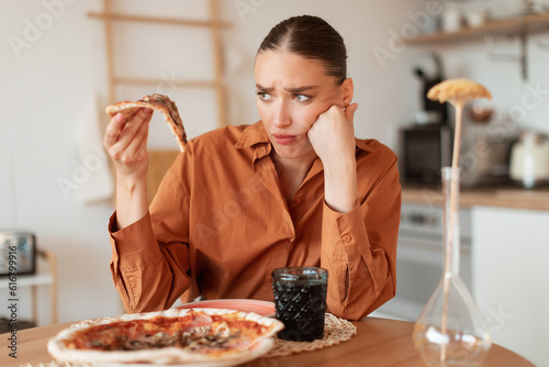 Foto Upset woman looking at delicious piece of high-calorie pizza, holding slice in h