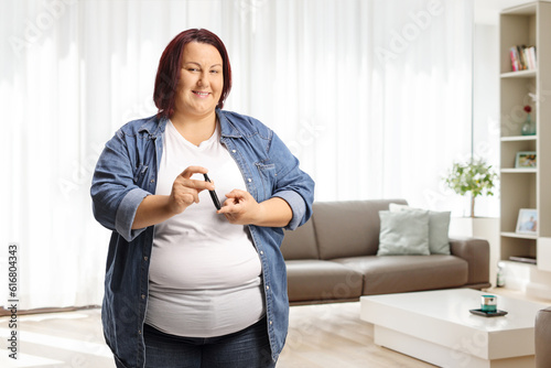 Overweight woman poking finger with an insulin pen at home and looking