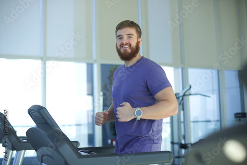 Happy young fit man training in the gym, running jogging on treadmill, doing cardio exercise and smile. Healthy lifestyle, sport, fitness concept