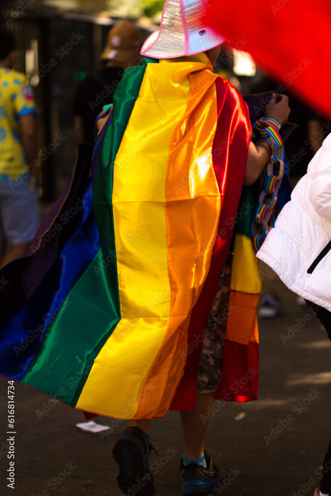 Vendedor ambulante na 27ª Parada do Orgulho LGBT+ vestido com a bandeira símbolo do orgulho gay. Avenida Paulista, São Paulo, Brasil. 