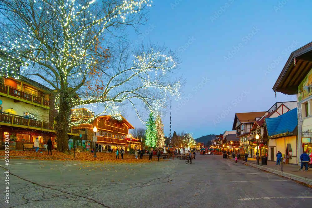 Visitors enjoy the colorful Bavarian themed village of Leavenworth, Washington, USA on a winter evening with lights coming on in the town.	