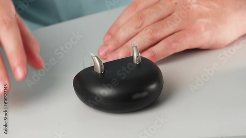 Patient charging hearing aid in special portable Smart Charger with built-in power bank. putting hearing aid into desktop charger