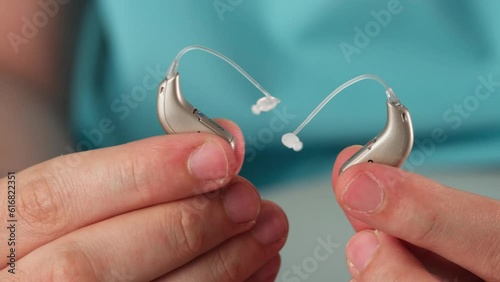 Hearing aids in hands making heart shape over blue background. Closeup of listening device for people with hearing disorder, disfunction. Technology that gives better sense of sound, speach