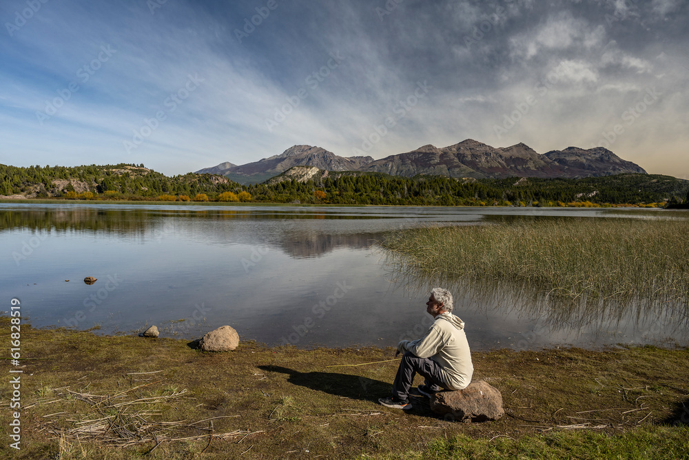 Man sitting on a rock reflects while contemplating an impressive landscape with a river and mountains. Man sitting on a rock reflects while contemplating an impressive landscape with a river and mountains.