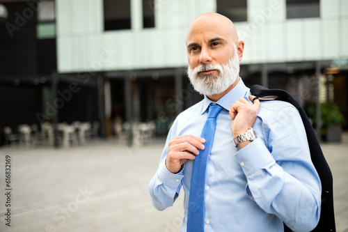 Mature bald stylish business man portrait with a white beard outdoor holding his jacket