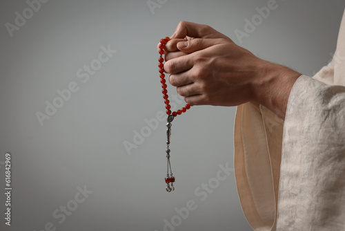 Muslim man with misbaha praying on light grey background, closeup. Space for text photo