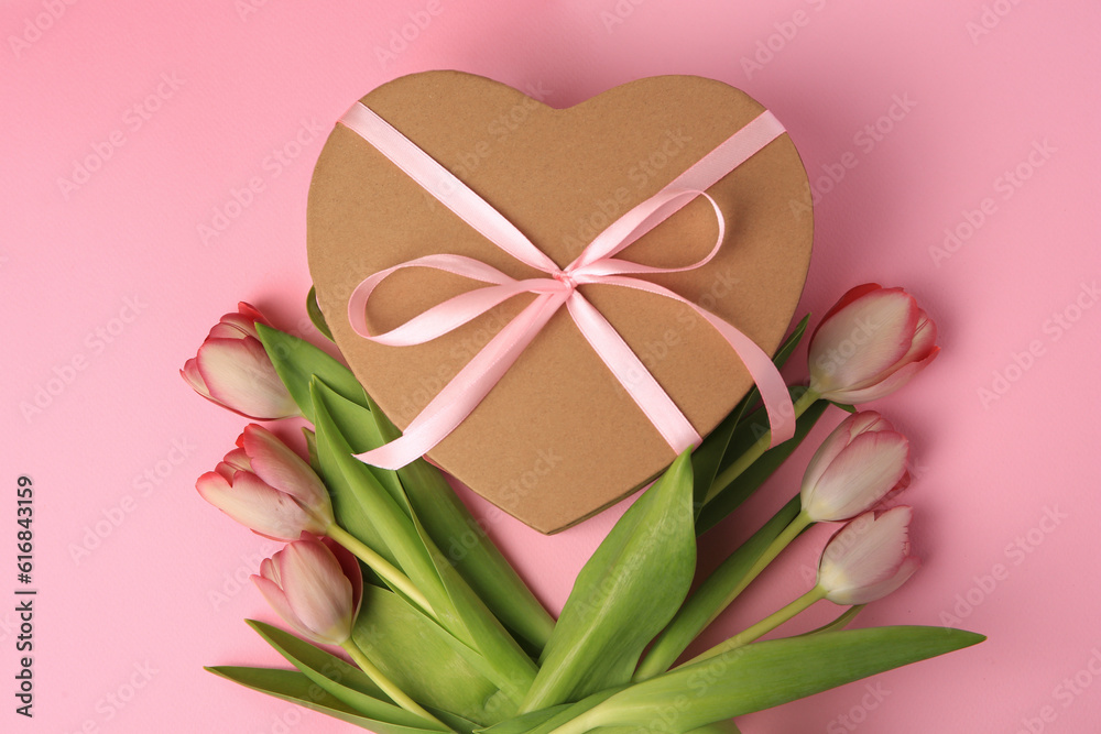Heart shaped gift box with bow and beautiful tulips on pale pink background, flat lay Heart shaped gift box with bow and beautiful tulips on pale pink background, flat lay