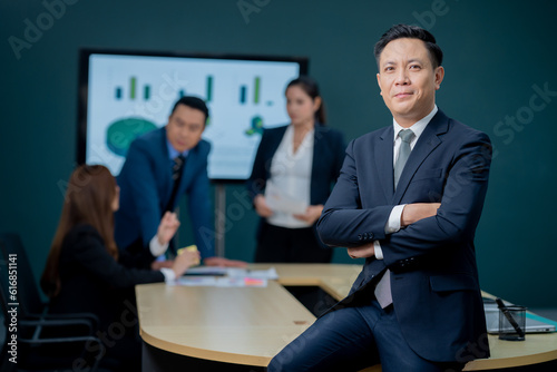 Handsome Asian middle-aged executives business man standing confident in the office in front of his team.