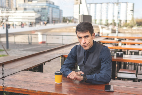 Canvas Print Business man sitting in a bar pointing at his watch looks disgusted at the camera