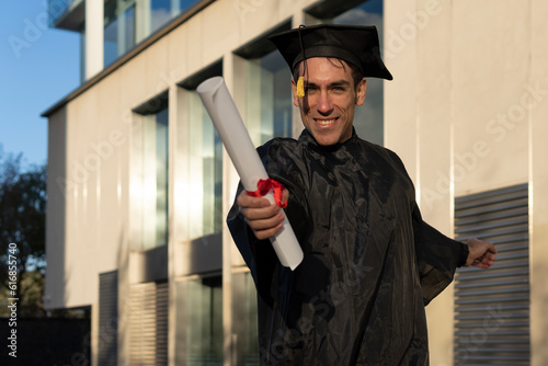 Man recent graduated, dressed in cap and gown, showing off his degree celebrating.