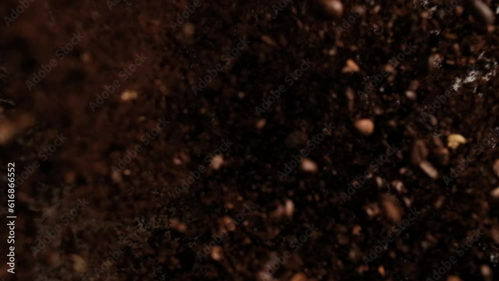 Slow-motion close-up of broken coffee beans and coffee powder splashing on dark background. High quality creative footage for promotional video editing