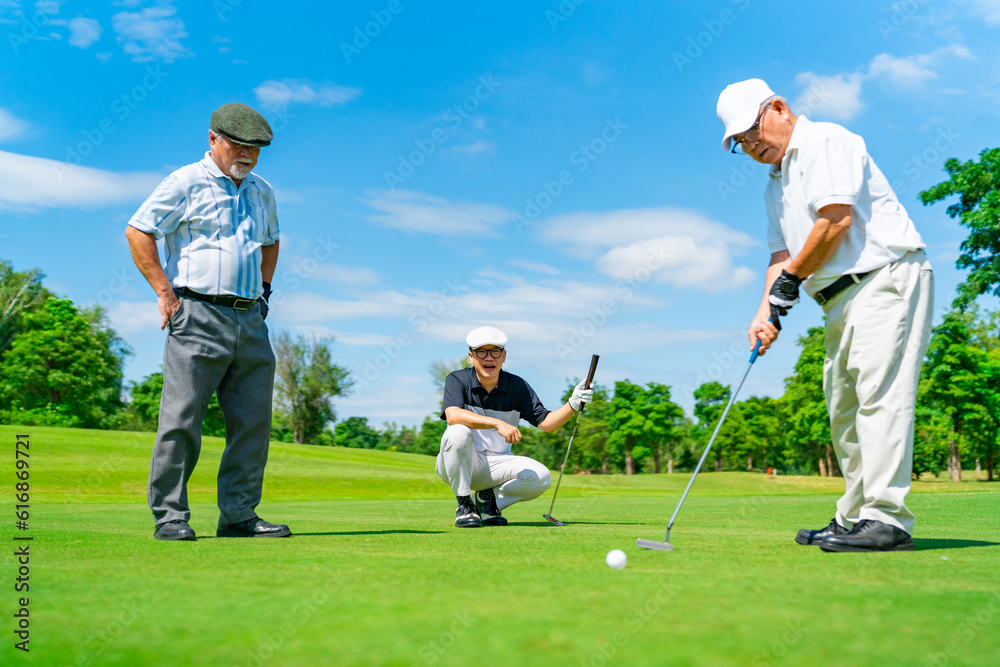 Obraz premium Group of Asian businessman and senior CEO golfing near the hole on golf fairway on summer holiday vacation. Healthy retired elderly people enjoy outdoor lifestyle and sport at golf course country club