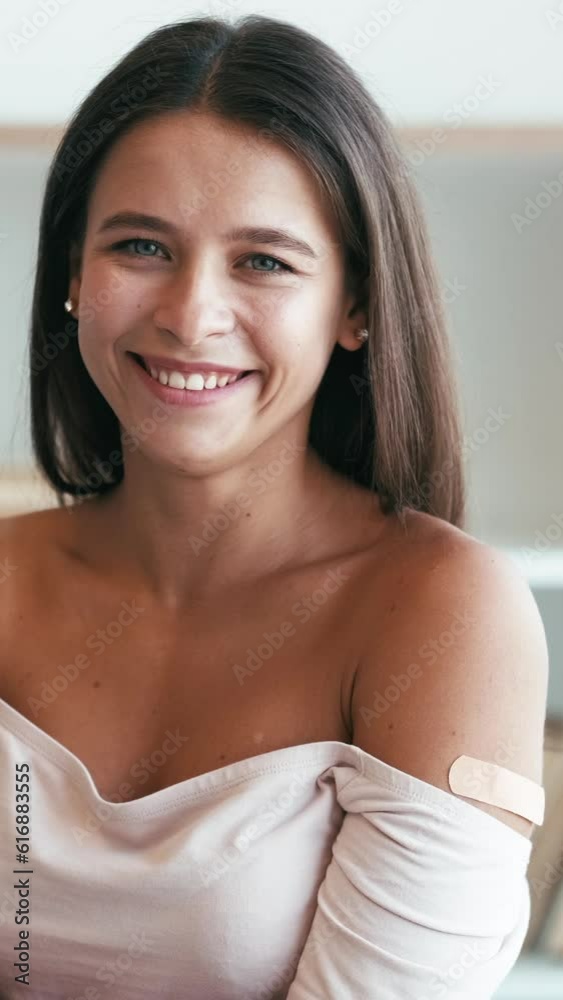 Vertical video. Infection prevention. Health protection. Disease spreading. Young happy smiling calm woman with patch on arm in medical face mask in light interior. Vertical video. Infection prevention. Health protection. Disease spreading. Young happy smiling calm woman with patch on arm in medical face mask in light interior.
