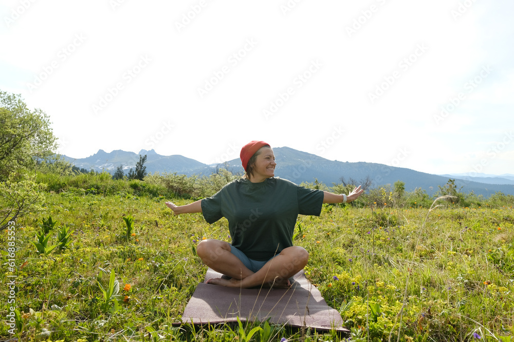 Woman doing yoga on blossom meadow and mountains background. Morning healthy activity.