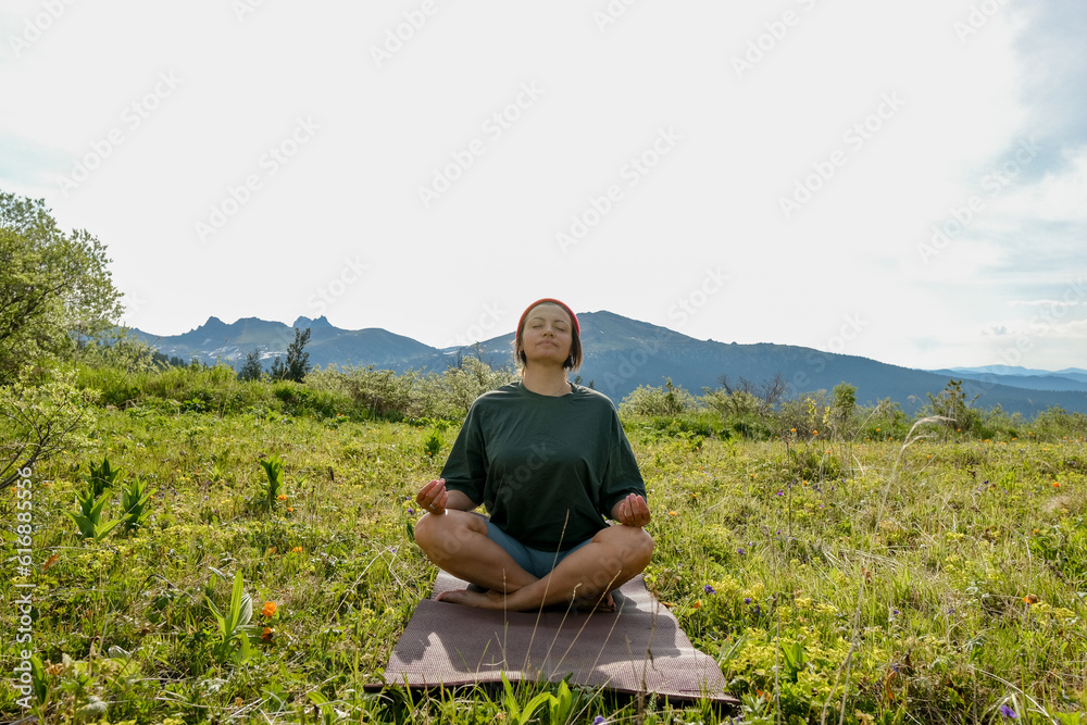 Wman doing yoga on blossom meadow and mountains background. Morning healthy activity.