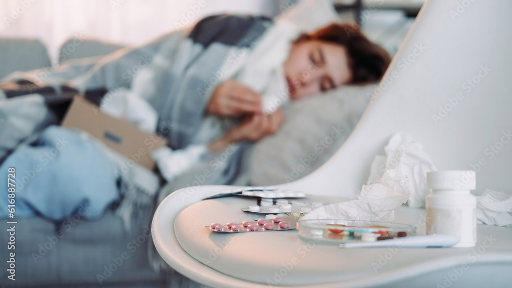 Home medicines. Healing pills. Variety of tablets flu treatment sick girl on blur laying on couch defocused background with free space.