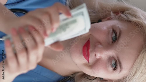 Vertical video. Medical corruption. Healthcare profit. Satisfied sneaky greedy female doctor counting cash money bribe 100 bill American US dollars banknotes.