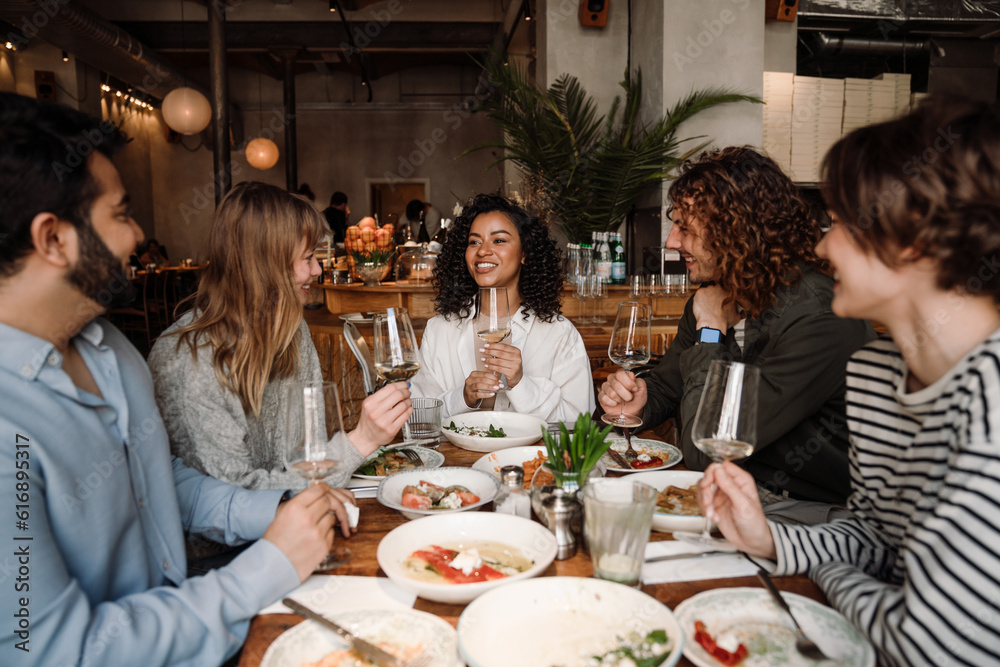 Group of cheerful friends talking and drinking wine while dining in restaurant