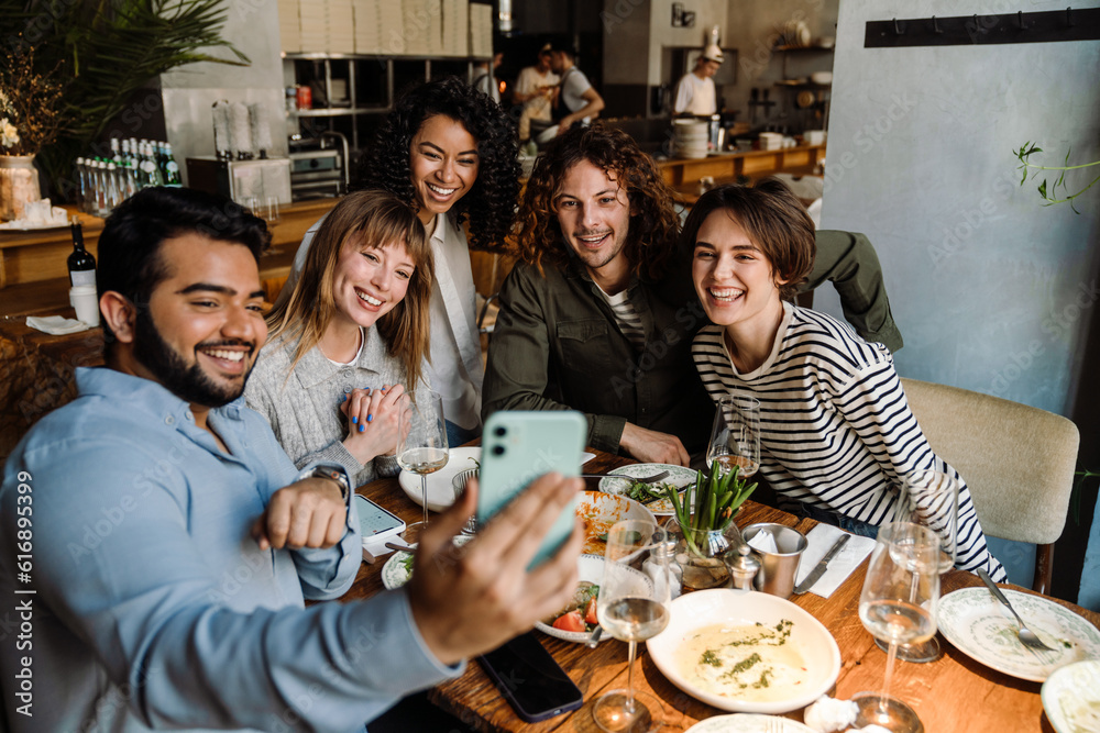 Group of joyful friends taking selfie while dining in restaurant